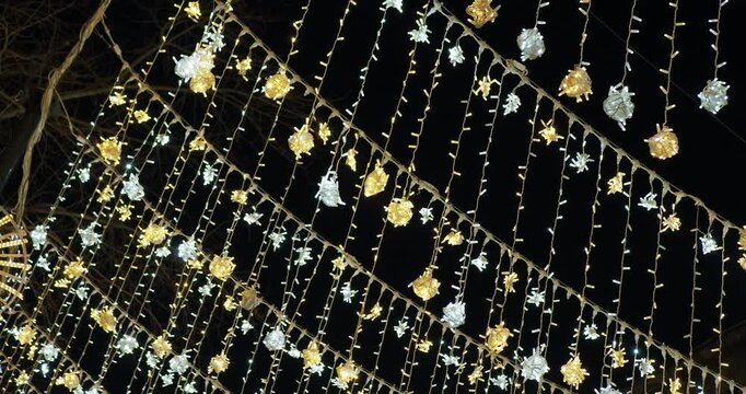 Holiday season. Many beautiful colorful garlands are hung above the street and glow in the dark, illuminating the sidewalk. The camera rotates. Hand held. Siberia.