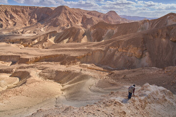 Majestic mountain landscape in the Nahal Ashosh Nature Reserve, Negev Desert. Orange sandstone hills and mountain folds. Hikers in the trail less travelled. Active lifestyle. Outdoor vacation.