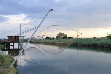 Fishermen's shack with fishing net on the Cervia salt marsh canal, Ravenna, Italy
