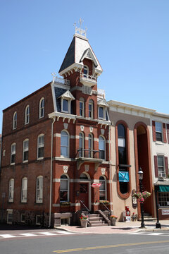 Narrow three story brick building with tall arched windows and small peaked tower room structure sitting high above the rest of the building 