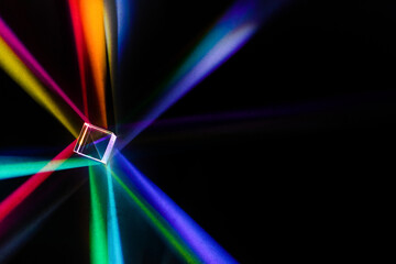 A glass dichroic prism disperse light into different colors on a black background