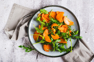 Close up of roasted sweet potato and fresh arugula salad on a plate on the table top view