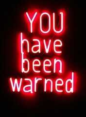 Obraz premium A neon sign with the words 'YOU have been warned' in white on red against a black background. The text is bold and illuminated by bright light from above.