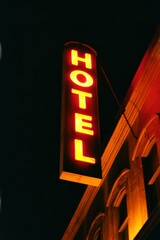 Night photography of a hotel sign 'HOTEL' glowing in orange light against a dark background.