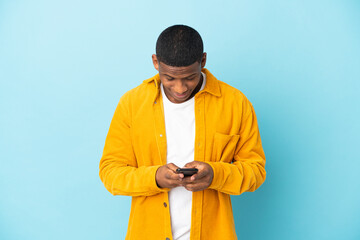 Young latin man isolated on blue background sending a message with the mobile
