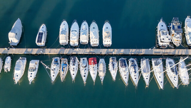 A breathtaking top-down aerial view of a marina with rows of luxury yachts and sailboats neatly docked along a wooden pier. 