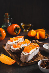 Sandwiches on rye ciabatta with ricotta, persimmon, honey and nuts on a board vertical view