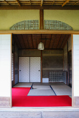 A serene Japanese room with tatami mats, wooden beams, sliding doors, and a red carpet. The simple...