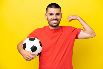 Young caucasian man playing soccer isolated on yellow background doing strong gesture