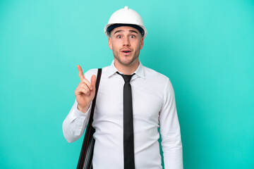 Young architect caucasian man with helmet and holding blueprints isolated on blue background intending to realizes the solution while lifting a finger up