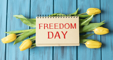 Freedom Day text on notepad which flower on wooden background