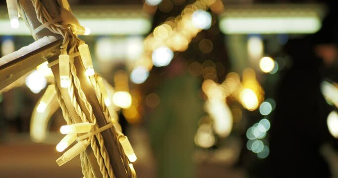 Holiday season. People are walking next to a Christmas tree and beautiful installations with iridescent multicolored lights against the background of a building with an illuminated facade. Hand held. 
