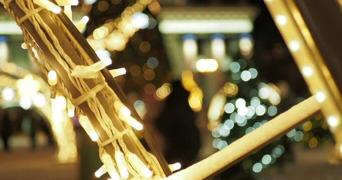 A man throws a child up to bring him joy next to a Christmas tree and beautiful installations of iridescent multicolored lights. Hand held. Siberia. Out of focus.