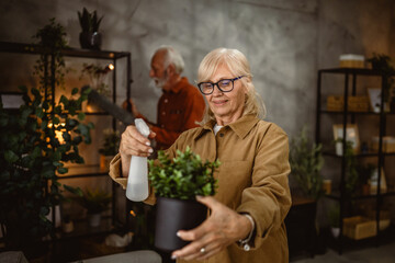 senior woman take care of home plants and use spray to hydration