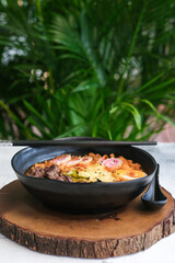 A beautifully assembled ramen bowl featuring tender meat, a soft-boiled egg, melted cheese, and vegetables, complemented by a spicy and creamy broth