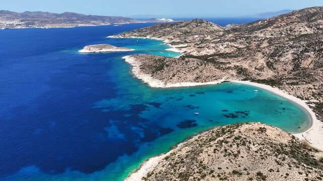 Aerial drone cinematic video of paradise blue bay of uninhabited island of Polyaigos with turquoise crystal clear sea visited by luxury yachts and sail boats resembling a blue lagoon, Cyclades, Greece
