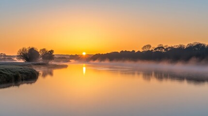 Misty sunrise over calm river reflecting golden sunlight.
