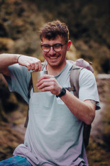 A man wearing glasses and carrying a backpack is happily drinking from a cup