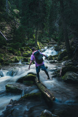 A man carrying a backpack carefully crosses over a river on a log
