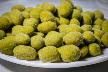 A close-up view of bright yellow-green wasabi-flavored nuts coated in a fine powder, creating a spicy and crunchy snack. Blurred background for emphasis.

