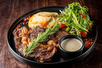 A delicious plate featuring succulent grilled steak garnished with fresh rosemary. Accompanied by creamy mashed potatoes, a fresh salad, and a side of savory sauce. Perfect for food lovers.