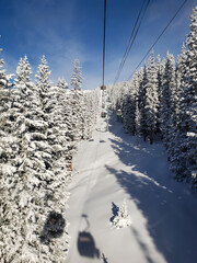 Above from the chairlift cable car, ski resort in the rocky mountains. Blue sky, wispy clouds. Trees covered in powder snow.