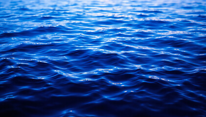 Rippling blue water surface with varying shades of blue and reflections of light creates a shimmering effect at dawn .