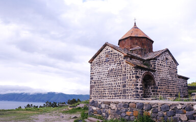 A picturesque stone church is beautifully located beside the lake, showcasing a stunning view beneath a cloudy sky