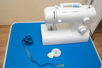 A sewing machine stands on a table with sentimental paper, chalk and pins, against the background of women's clothing and a black mannequin for cutting and sewing.