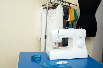 A sewing machine stands on a table with sentimental paper, chalk and pins, against the background of women's clothing and a black mannequin for cutting and sewing.