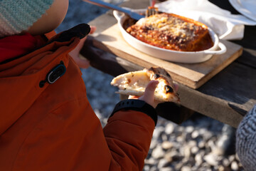 A child holding a slice of white pizza, with visible melted cheese and herbs. The candid moment captures a relaxed outdoor dining experience