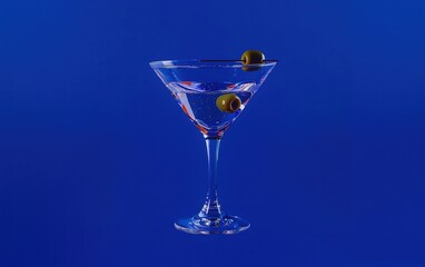 A martini glass floating mid-air with an olive garnish, on a deep blue background