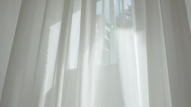 Transparent blurred white silk soft fabrics floating with sunlight shining through, shadows reflected on the textile surface, close up.