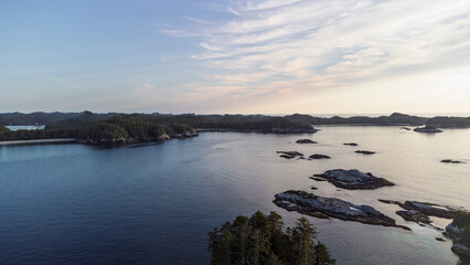Small islands sit in a the calm ocean as the yellow light of the sun setting creeps across the sky. 