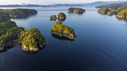 Heavily forested islands dot a narrow straight on a calm day with mountains in the background. Taken near Calvert Island, British Columbia, Canada