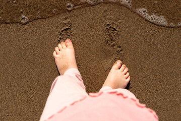 Child stand feet on sand beach, top view of girl feet in sea wave, childhood
