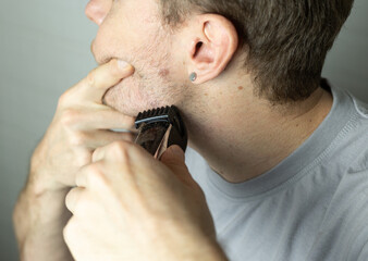 A man trims his beard with a trimmer. An electric razor trimming a beard. Beard care at home.