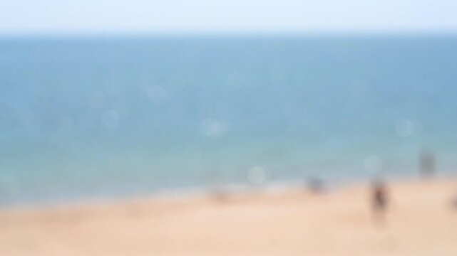 Blurred background. People resting and sunbathing on sandy beach of sea shore near calm blue sea with white bokeh spots from sun glare from ripples on water on sunny summer day. Natural seascape