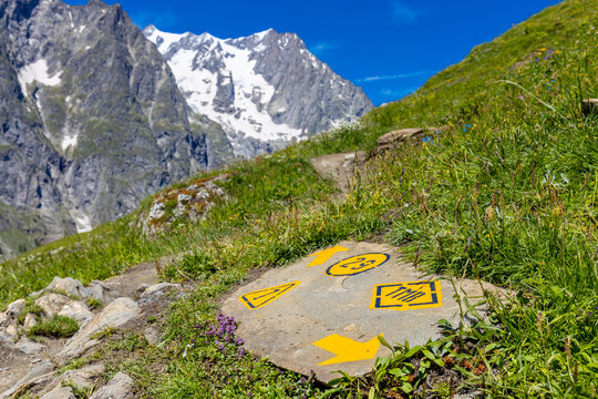 TMB Tour du Mont Blanc arrow and pointing sign on the hiking path in the Alps. Trekking around Montblanc in summer beautiful landscape of the alpine green meadows and high mountains covered with snow