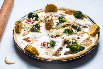 Raw Quiche with broccoli, corn, chicken and tomatoes is ready to bake in the oven. Raw pie on a white table