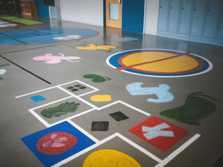 Piso de concreto en una escuela. Hay varios juegos pintados en el suelo, entre ellos la rayuela y los cuatro cuadrados
