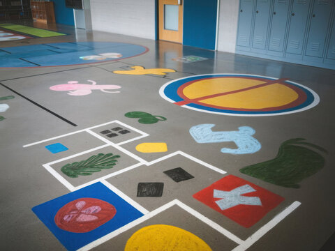 Piso de concreto en una escuela. Hay varios juegos pintados en el suelo, entre ellos la rayuela y los cuatro cuadrados
