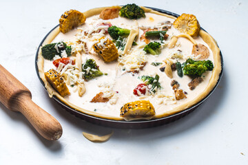 Raw Quiche with broccoli, corn, chicken and tomatoes is ready to bake in the oven. Raw pie on a white table