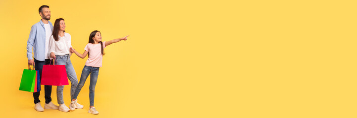 Obraz premium Family Shopping. Happy Parents And Little Daughter Holding Shopper Bags, Pointing Finger Aside At Copy Space, Asking Mom And Dad To Buy Something, Showing Great Offer Over Yellow Backdrop, Panorama