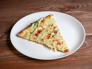 close-up of one piece of pizza on a white plate. Wooden table