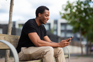 Smiling man using smartphone while sitting on outdoor bench