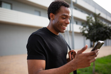 African American man walking and smiling while using smartphone