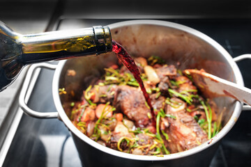Pouring red wine into a stainless steel pot to deglaze the roasted ingredients such as meat, vegetables and herbs, cooking a tasty stew, selected focus