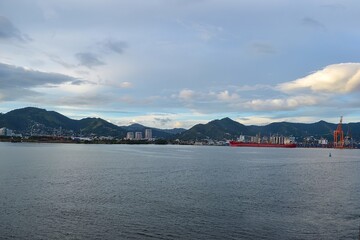 Coastal Cityscape with Mountain Range and Red Cargo Ship in Harbor