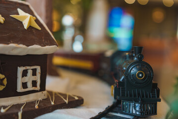 A detailed model train set and gingerbread house with icing and star decoration, set against a blurred background of colorful Christmas lights in London.